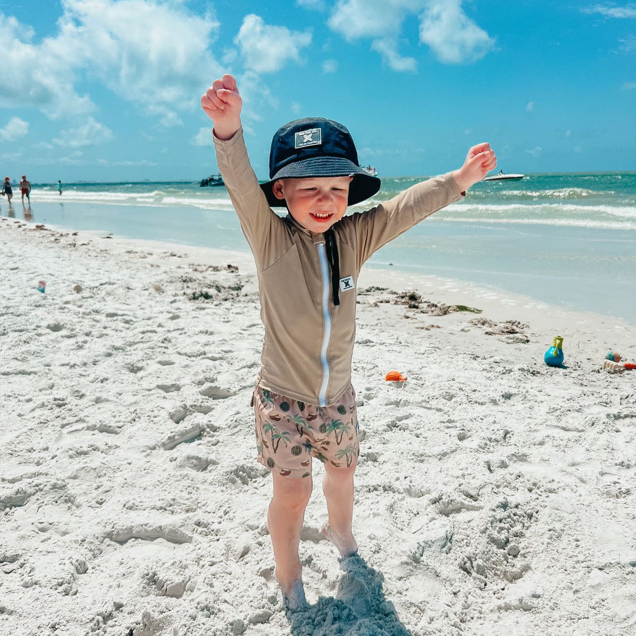 fun in the sun wearing Rad Toddlers 'Sand' Rashguard Shirt with front zipper and UPF 50+ protection, perfect for pairing with board shorts for water activities.