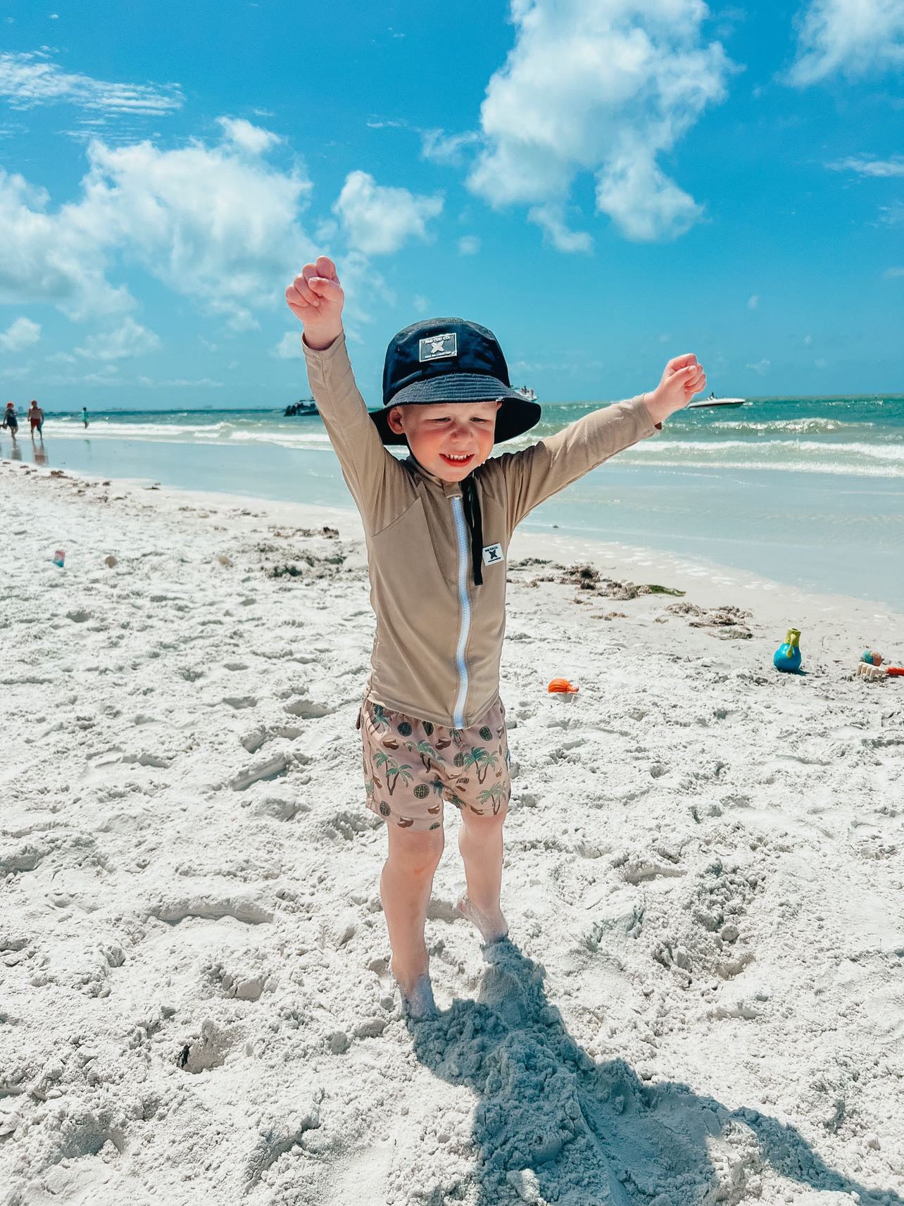 fun in the sun wearing Rad Toddlers 'Sand' Rashguard Shirt with front zipper and UPF 50+ protection, perfect for pairing with board shorts for water activities.