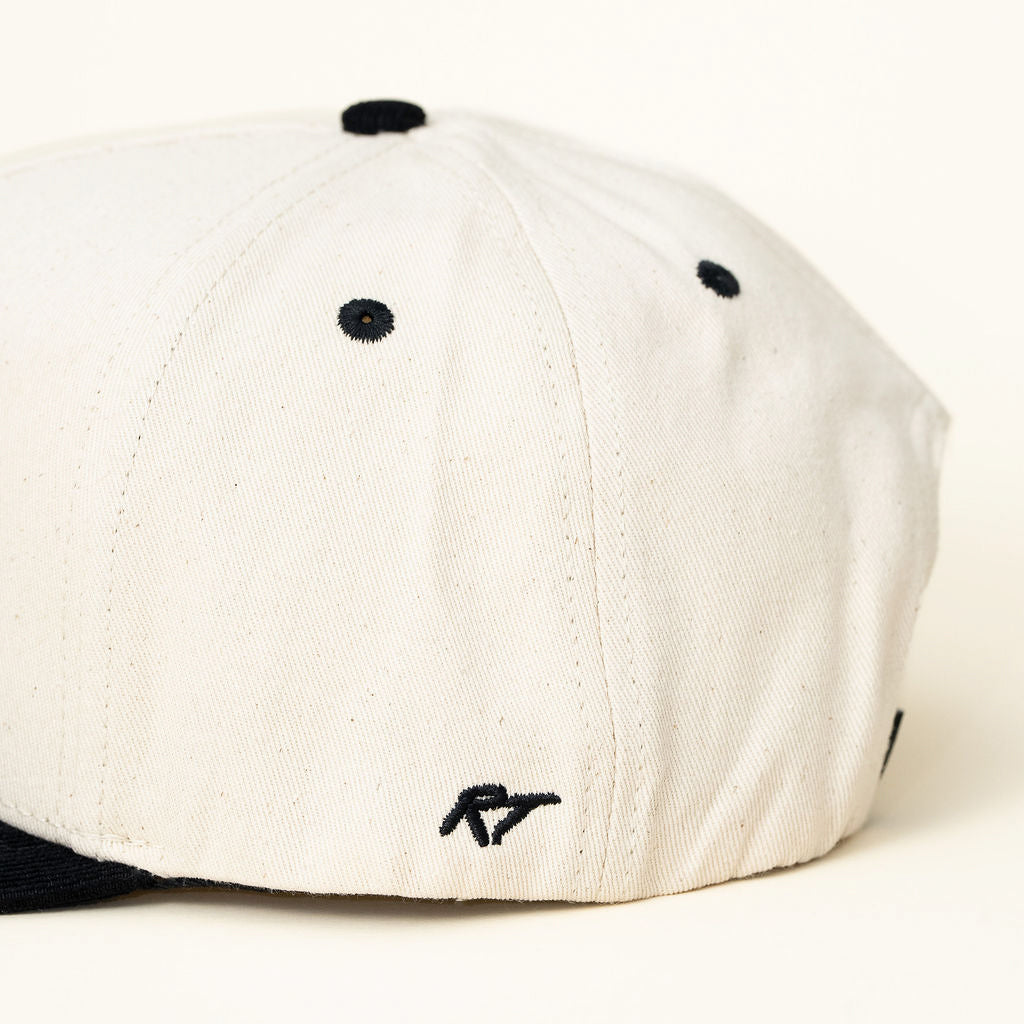 Side view of kids snapback showing the playful embroidered text on off-white and black hat.