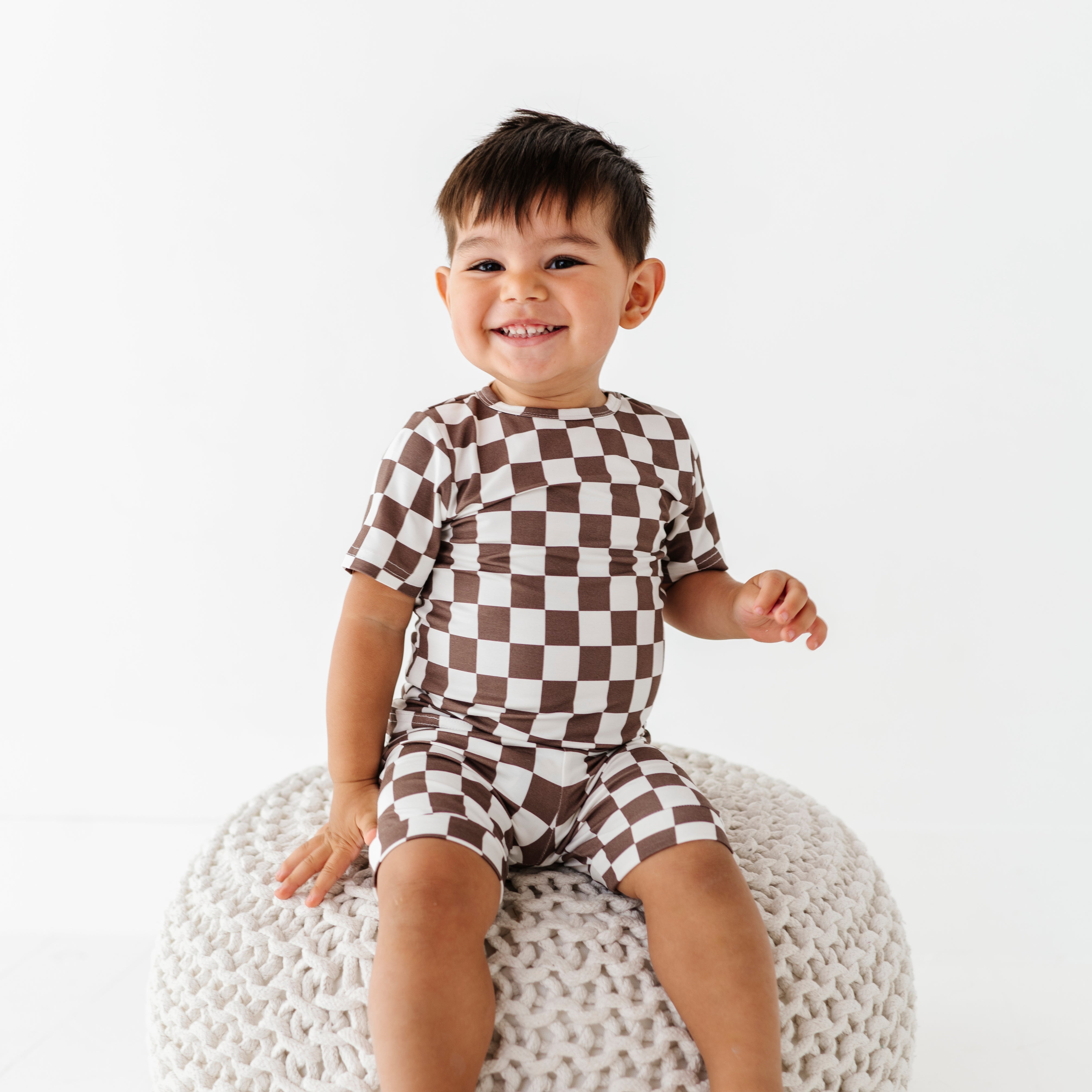 boy siting and smiling while wearing Bronze and white checkered bamboo short sleeve pajama set for toddlers, featuring soft, breathable fabric and a stretchy waistband by Rad Toddler.