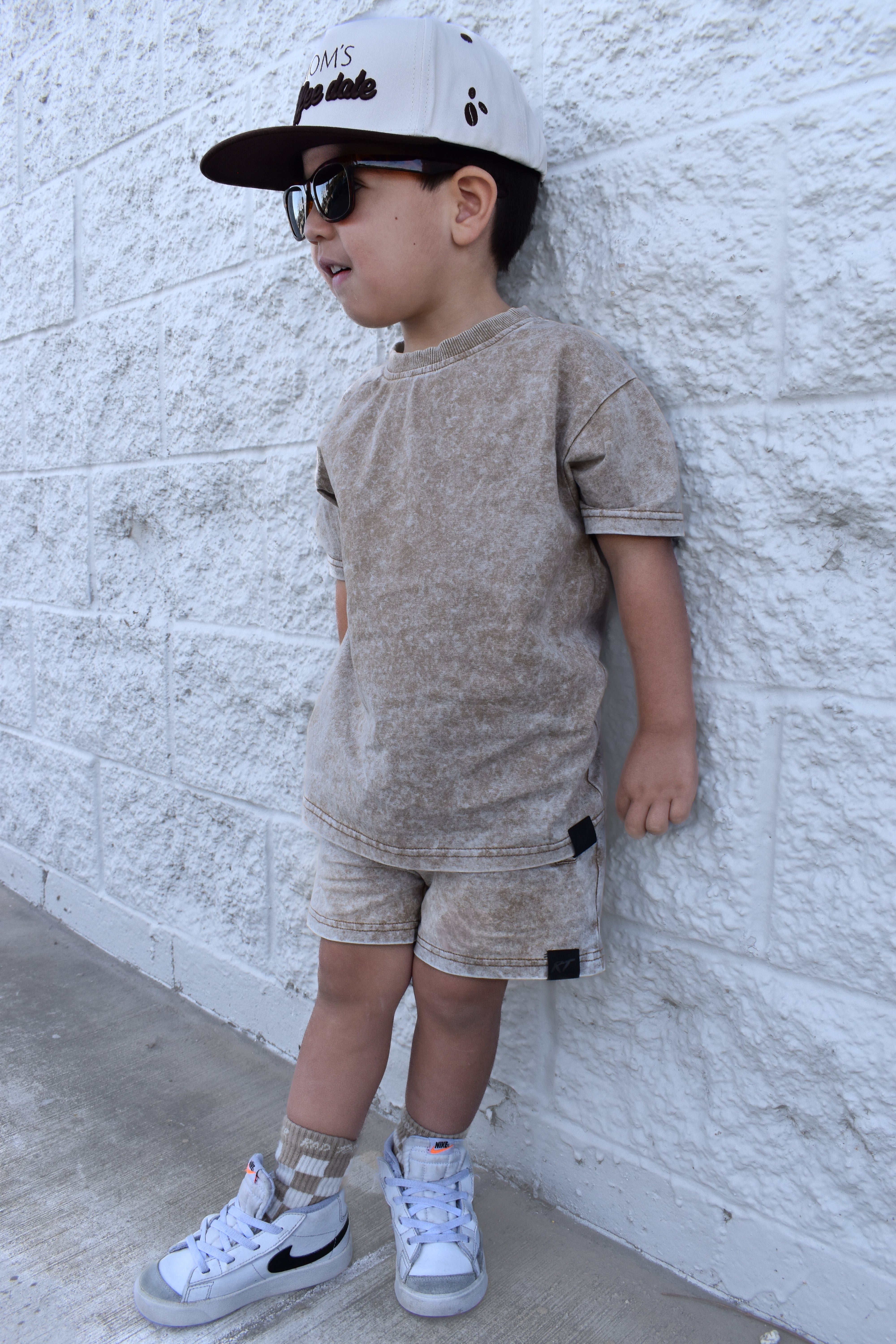 boy wearing stone washed sand set by Rad toddler while leaning against a wall and wearing glasses
