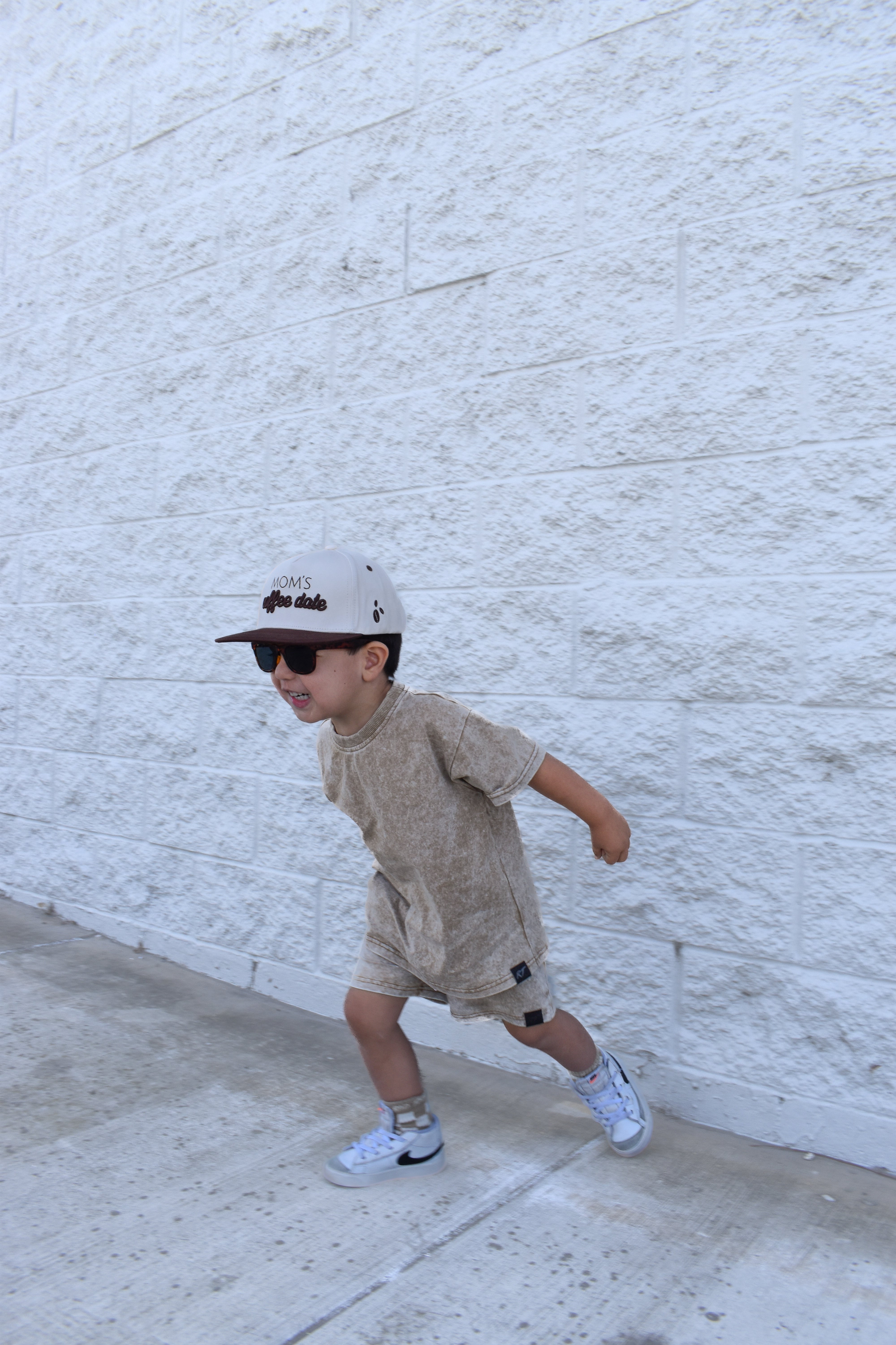 Child in stone wash sand set by rad toddler and cap against a white brick wall