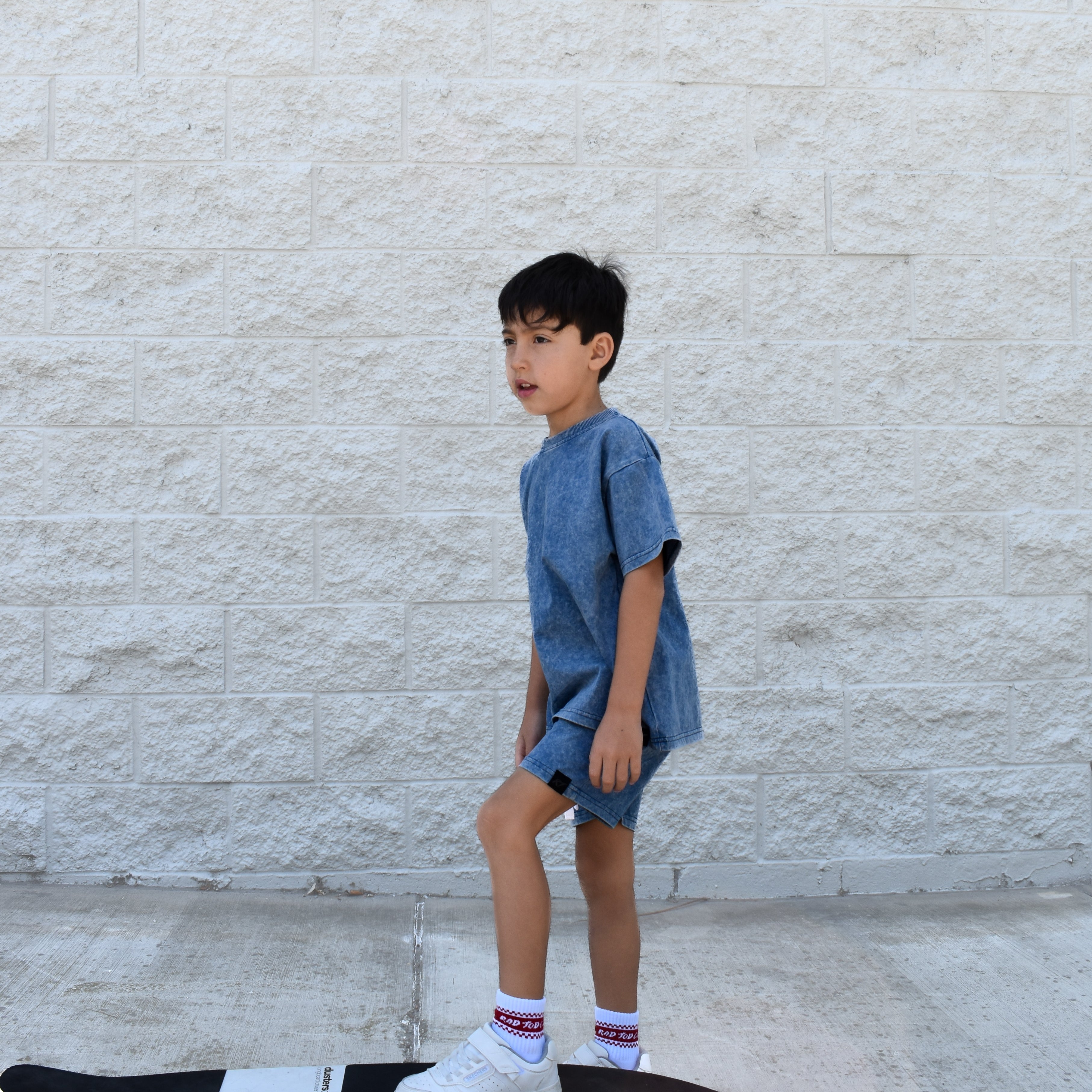 Child standing on a skateboard against a light-colored wall wearing vintage blue set