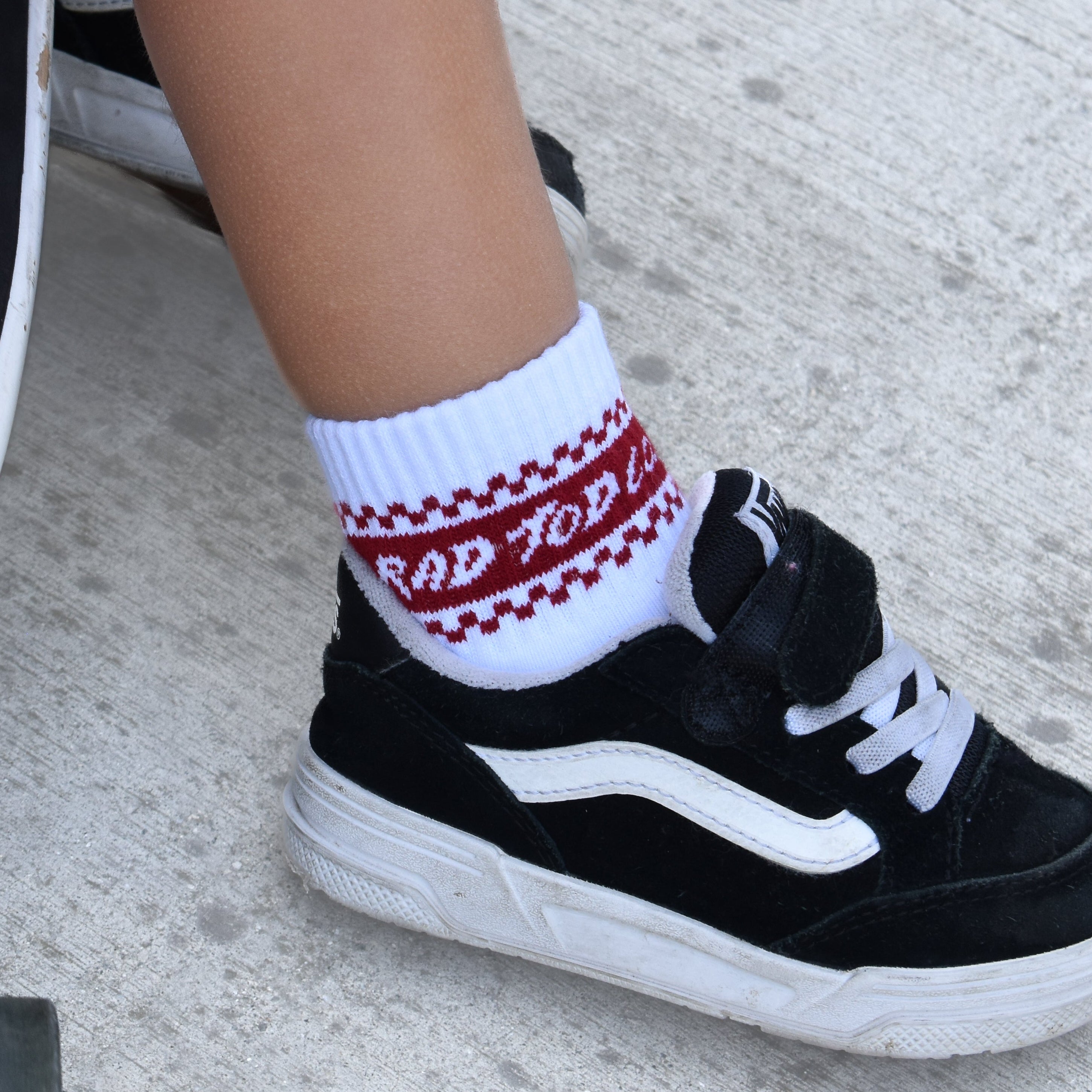 White toddler crew socks with red details and checker accents at the top in a vintage sporty style for kids.