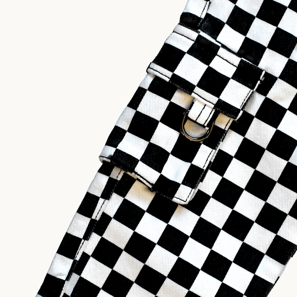 A close-up of a black and white checkered fabric accessory with a flap closure and metal snap hardware, photographed on a plain light background.