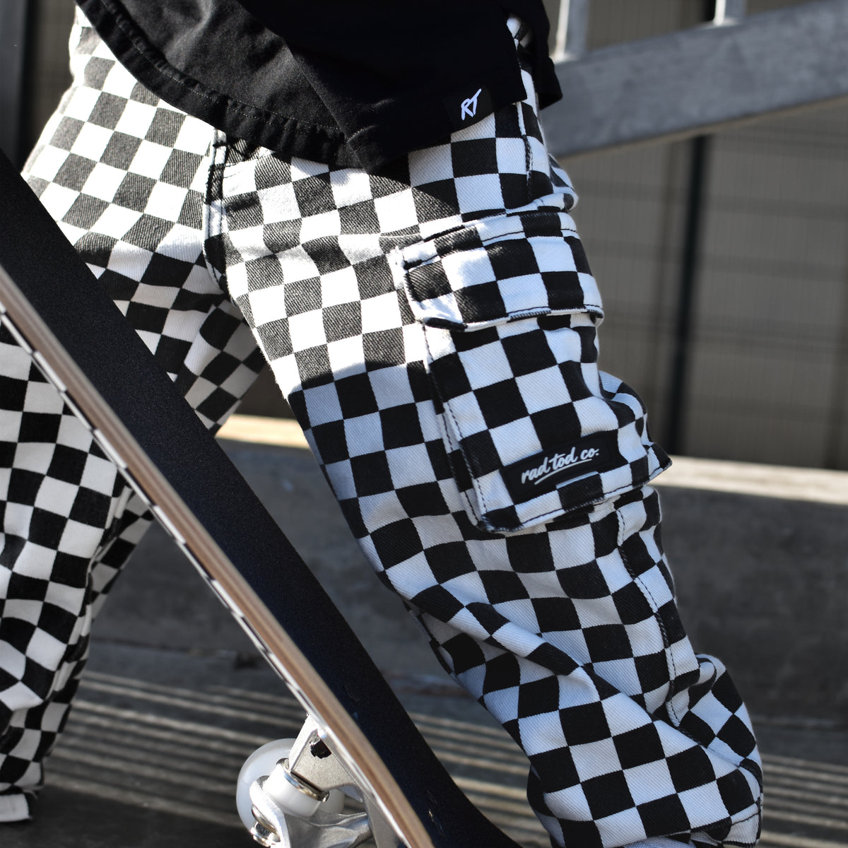 A person wearing black and white checkered cargo pants with a skateboard, captured in an outdoor urban setting.