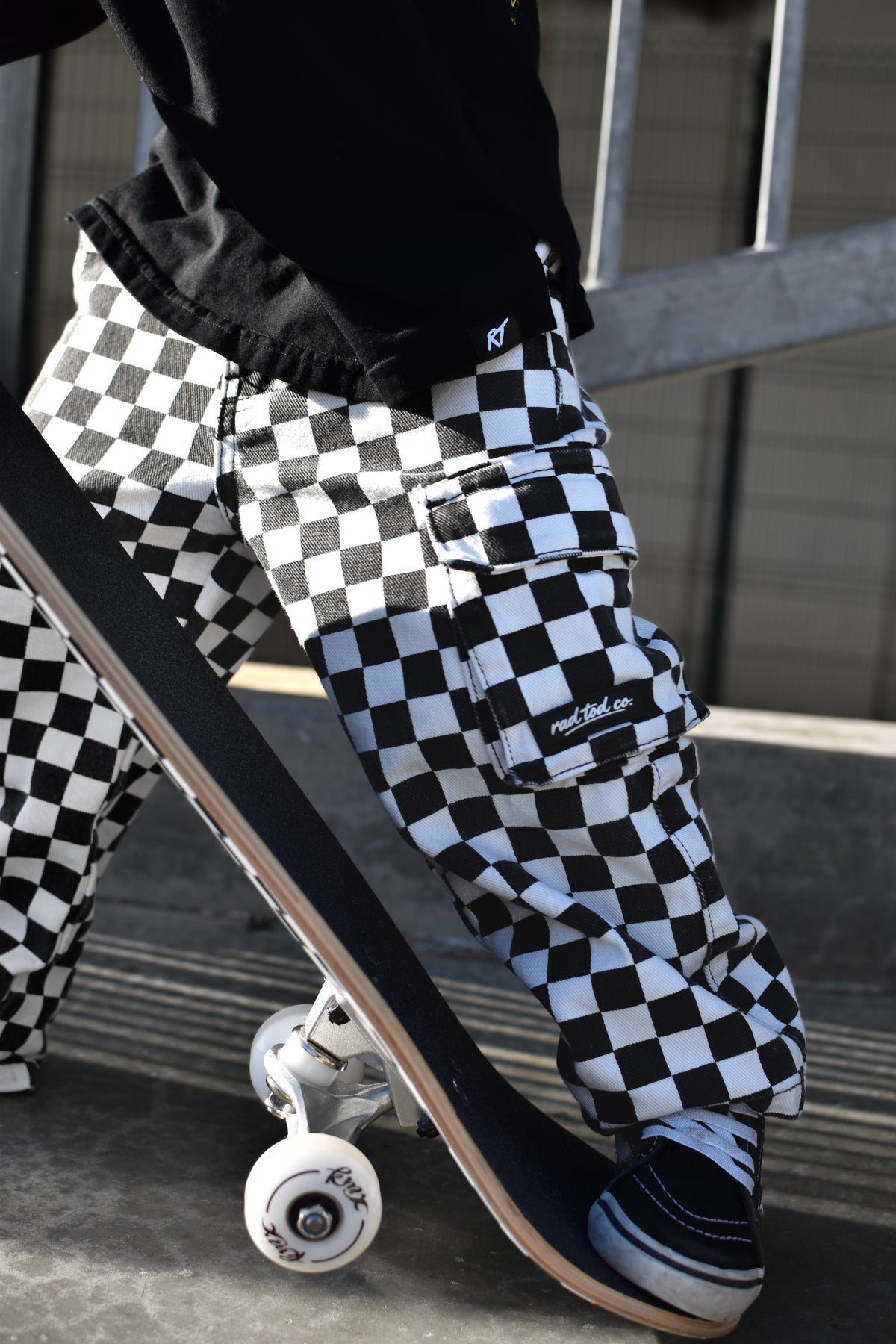 A person wearing black and white checkered cargo pants with a skateboard, captured in an outdoor urban setting.