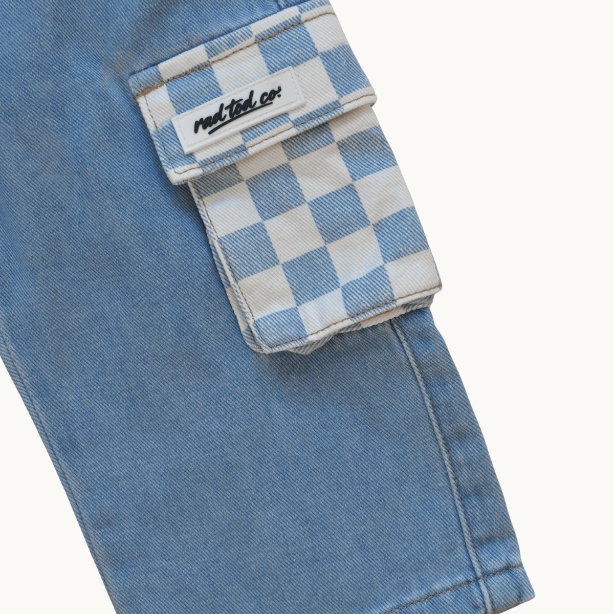 Close-up of a light blue denim cargo pocket with a blue and white checkerboard flap and a visible 'Rad Tod Co.' label.