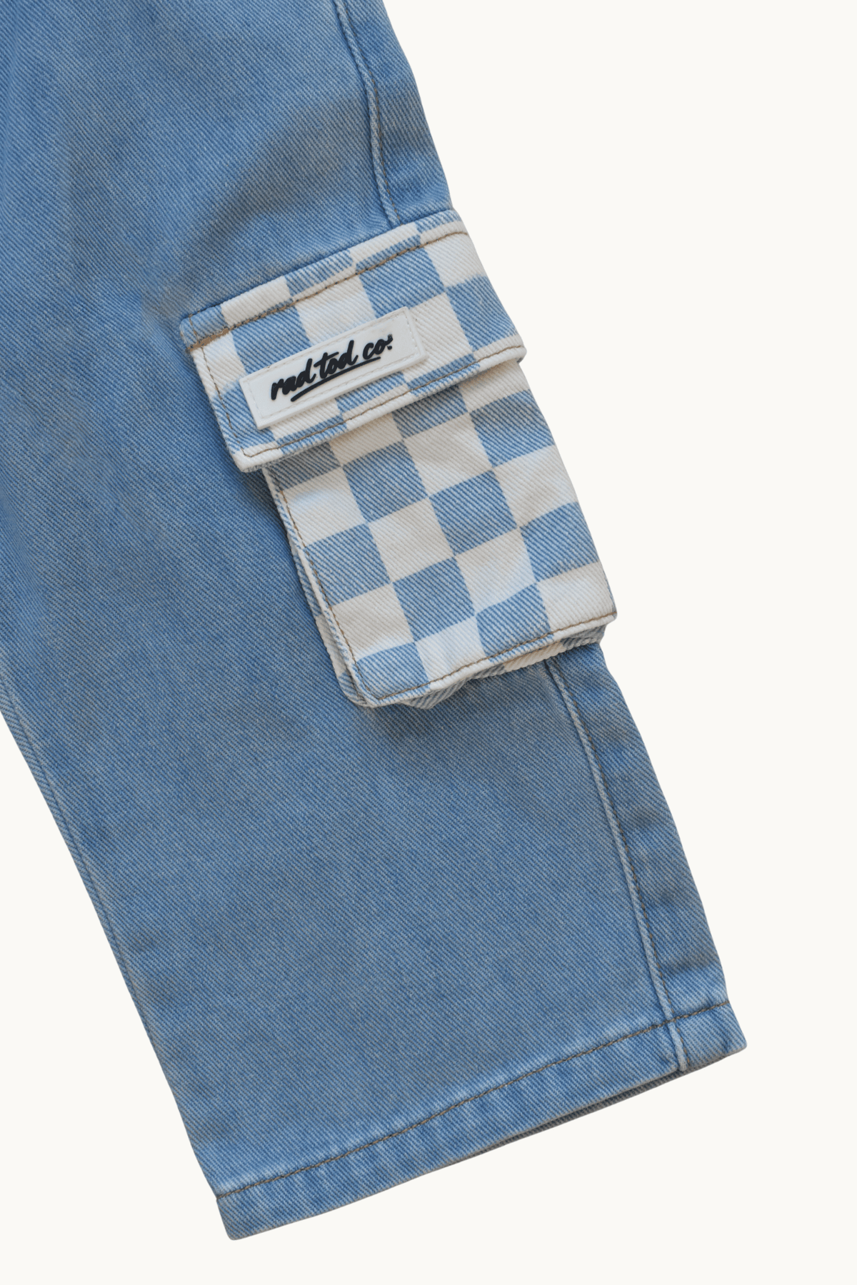 Close-up of a light blue denim cargo pocket with a blue and white checkerboard flap and a visible 'Rad Tod Co.' label.