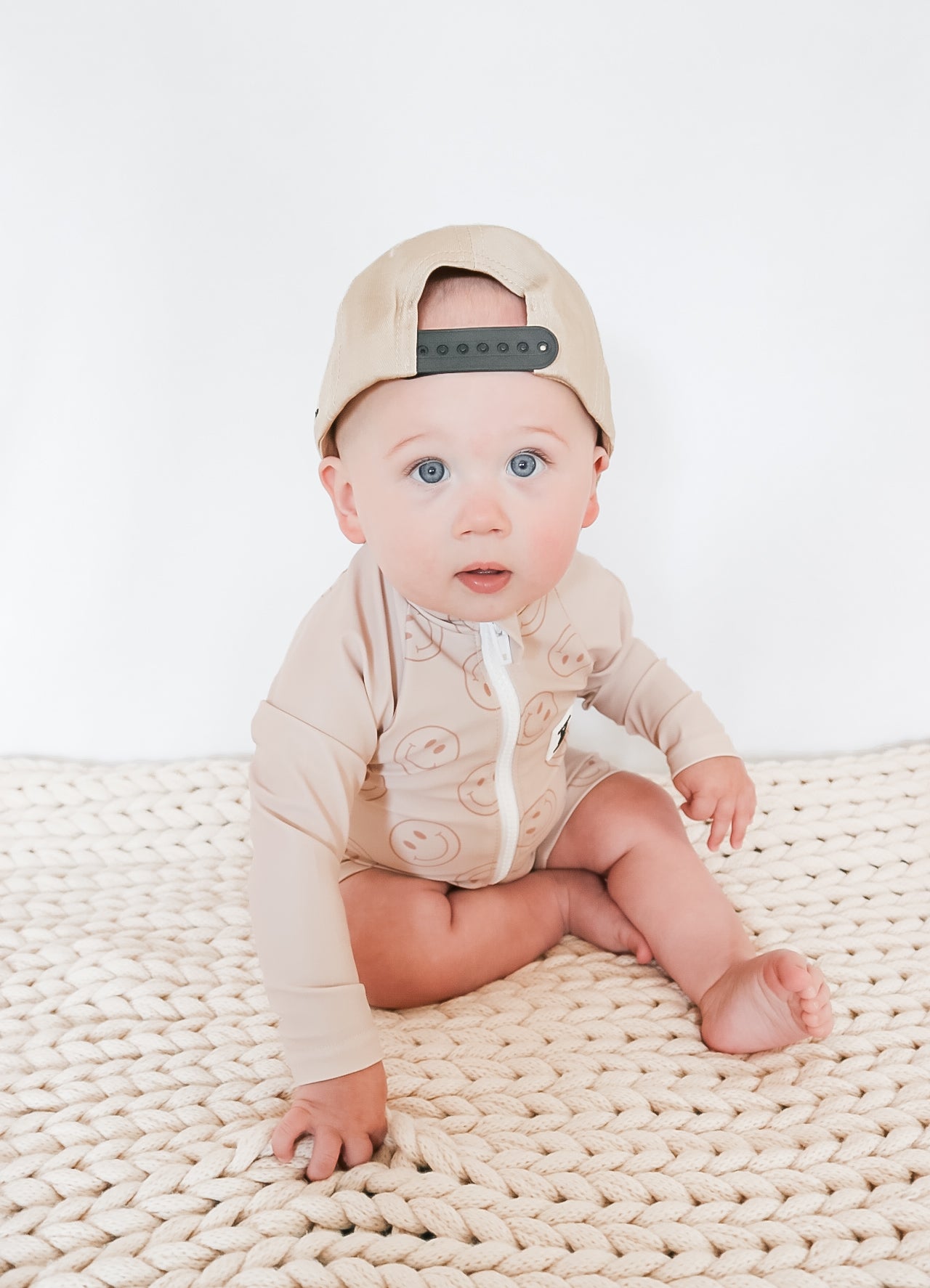 cute boy wearing Rad Toddlers Smiley Shore One-Piece Rashguard in beige with smiley face design, featuring easy zipper and UPF 50+ sun protection.