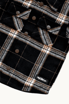Close-up of a black plaid flannel shirt jacket with brown buttons and a small 'RAD TOD co.' label near the bottom right, shown on a light background.