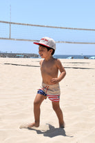 Child in swim trunks and cap on a sandy beach with ocean view