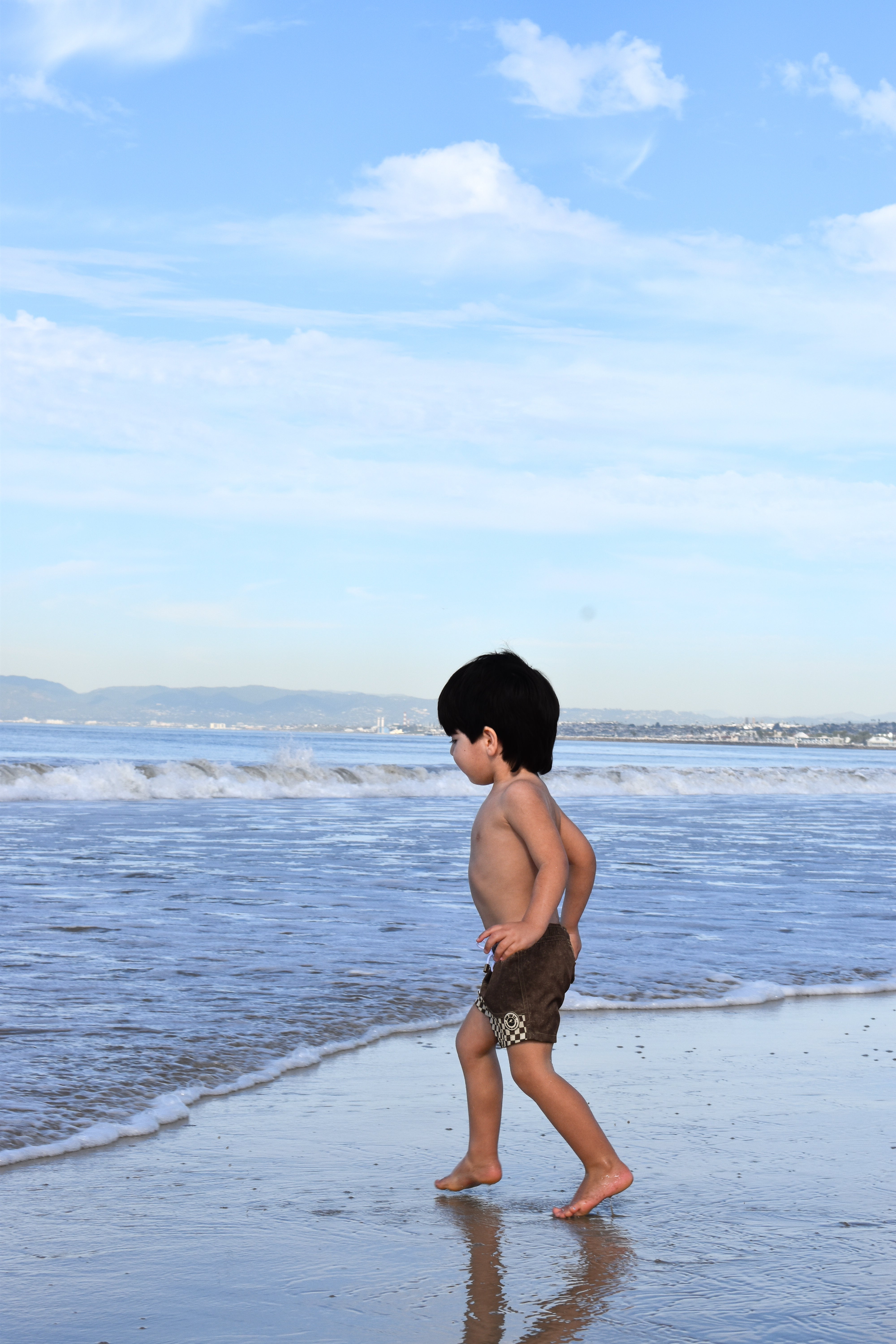 Child walking on a beach with clear blue sky and ocean waves.
