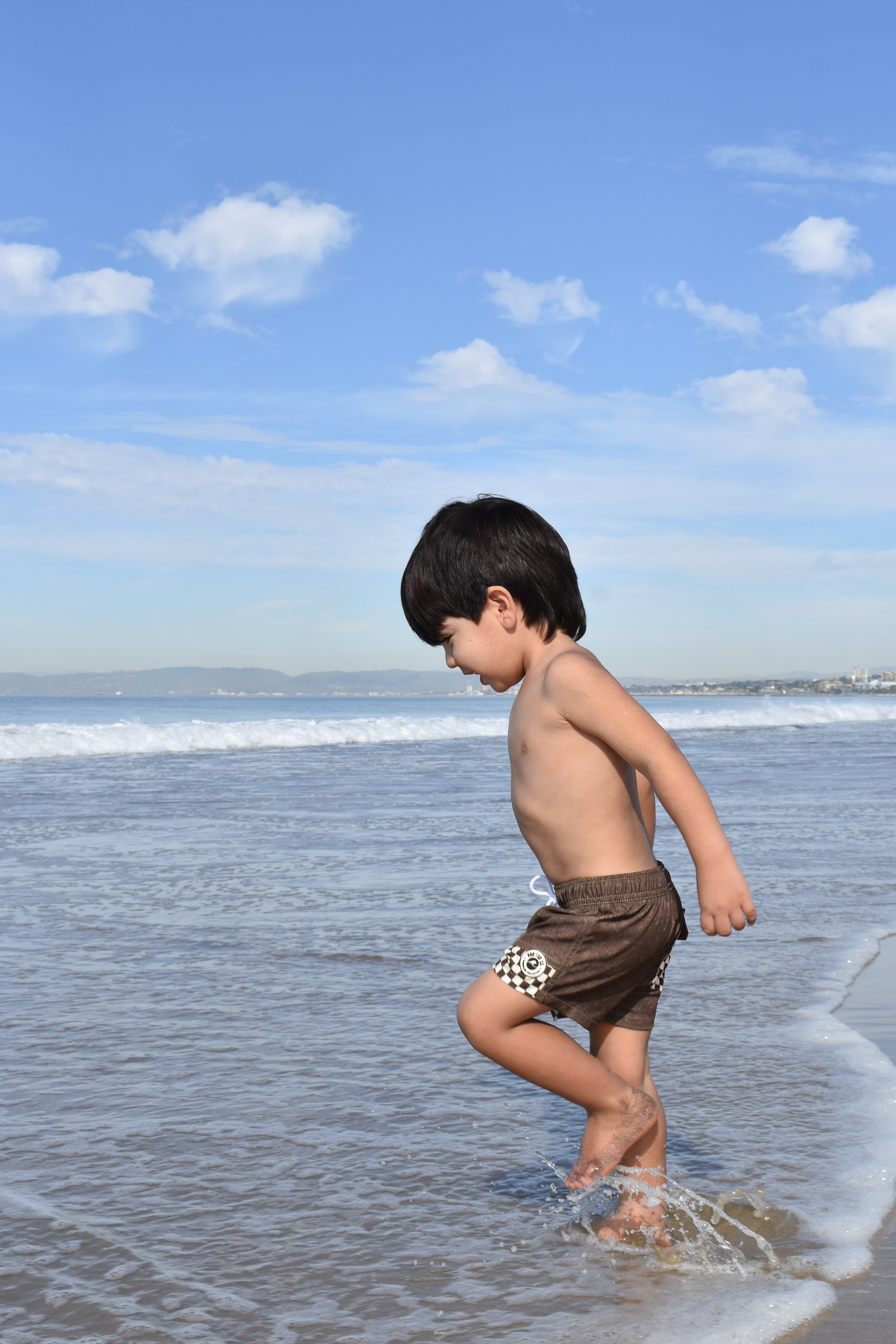 Child playing on a beach with waves and blue sky in the background