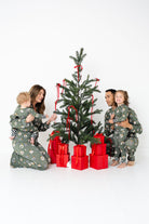 Family of four decorating a small Christmas tree with red ribbons and presents on a white background Christmas morning matching family bamboo pajamas for kids