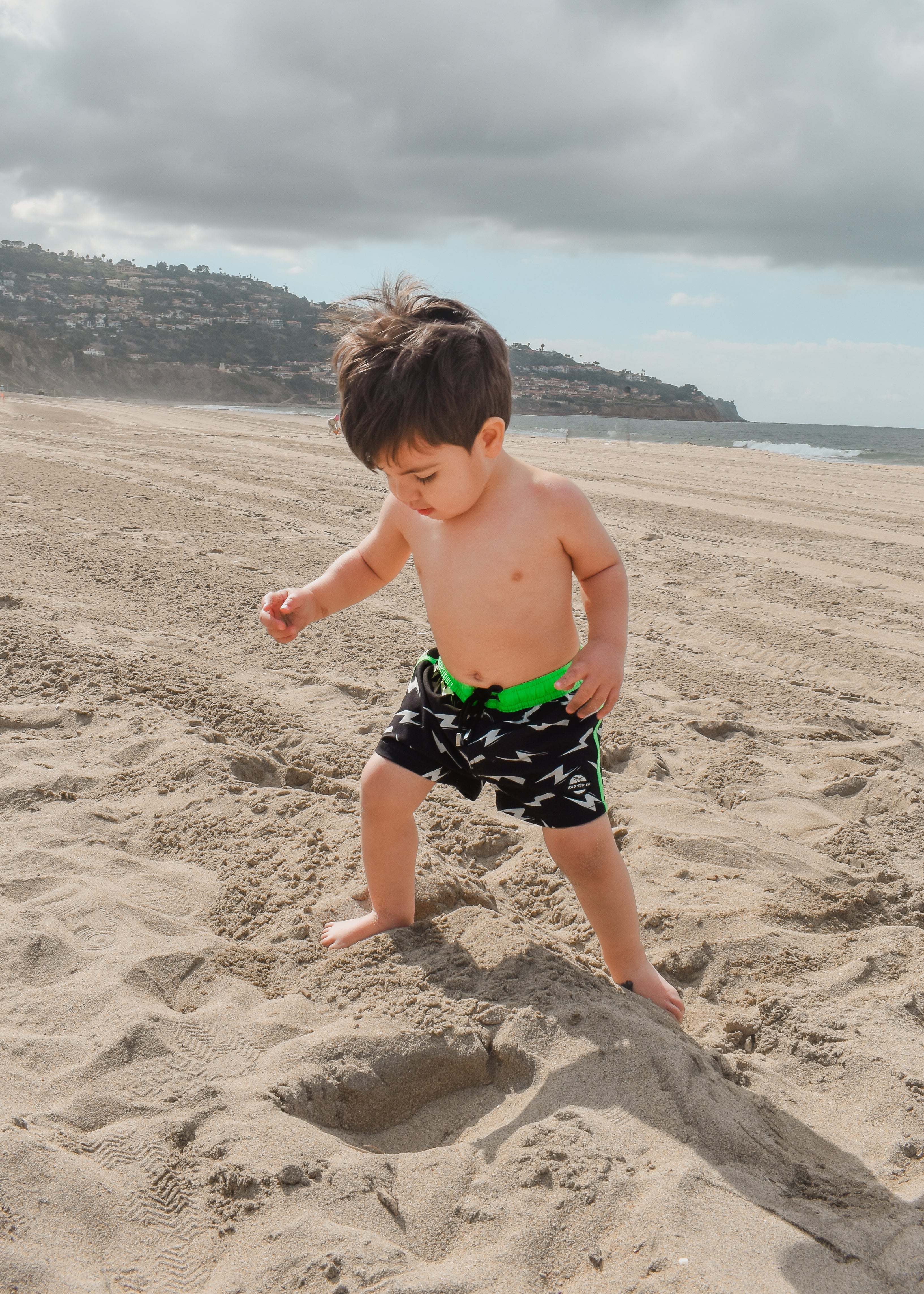 adventurous boy wearing Bright swim shorts with an elastic waistband and drawstring, made from quick-drying fabric. Ideal for swimming, beach trips, and outdoor activities. Features vibrant patterns and a comfortable fit for active kids.