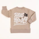 Beige crewneck sweatshirt with white ‘Have a Rad Day’ graphic, flag, smiley face, and checker details laid flat”