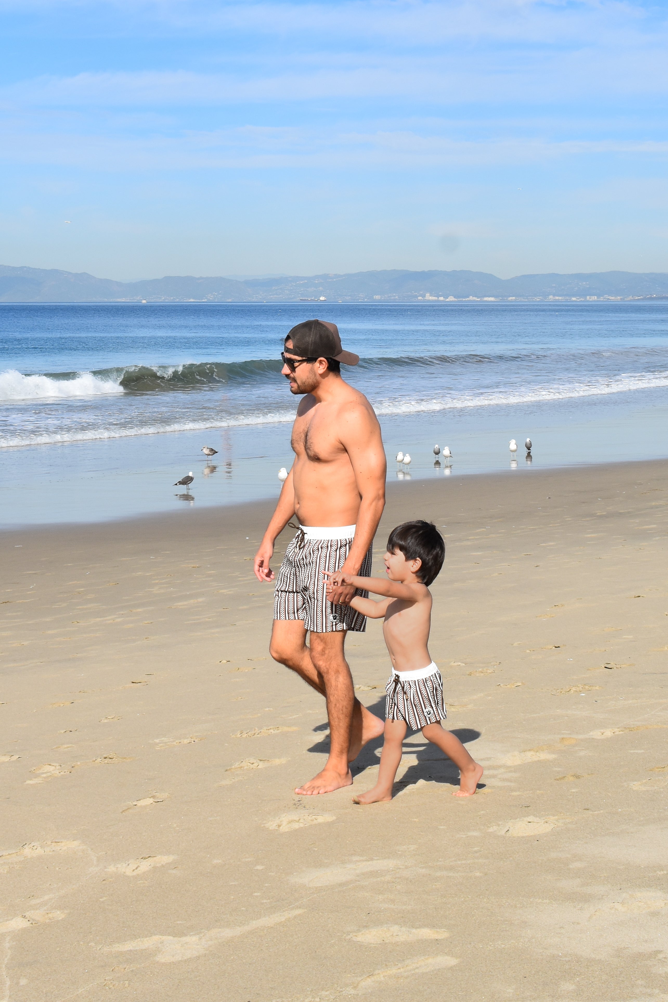 Man and child walking on a beach with ocean and sky in the background while matching in Rad Toddler Shorts
