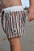 Child wearing Latte Stripes Swimmie with warm coffee-tone stripes on a beach by rad toddler