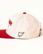 Beige cap with red brim and embroidered heart design on a white background