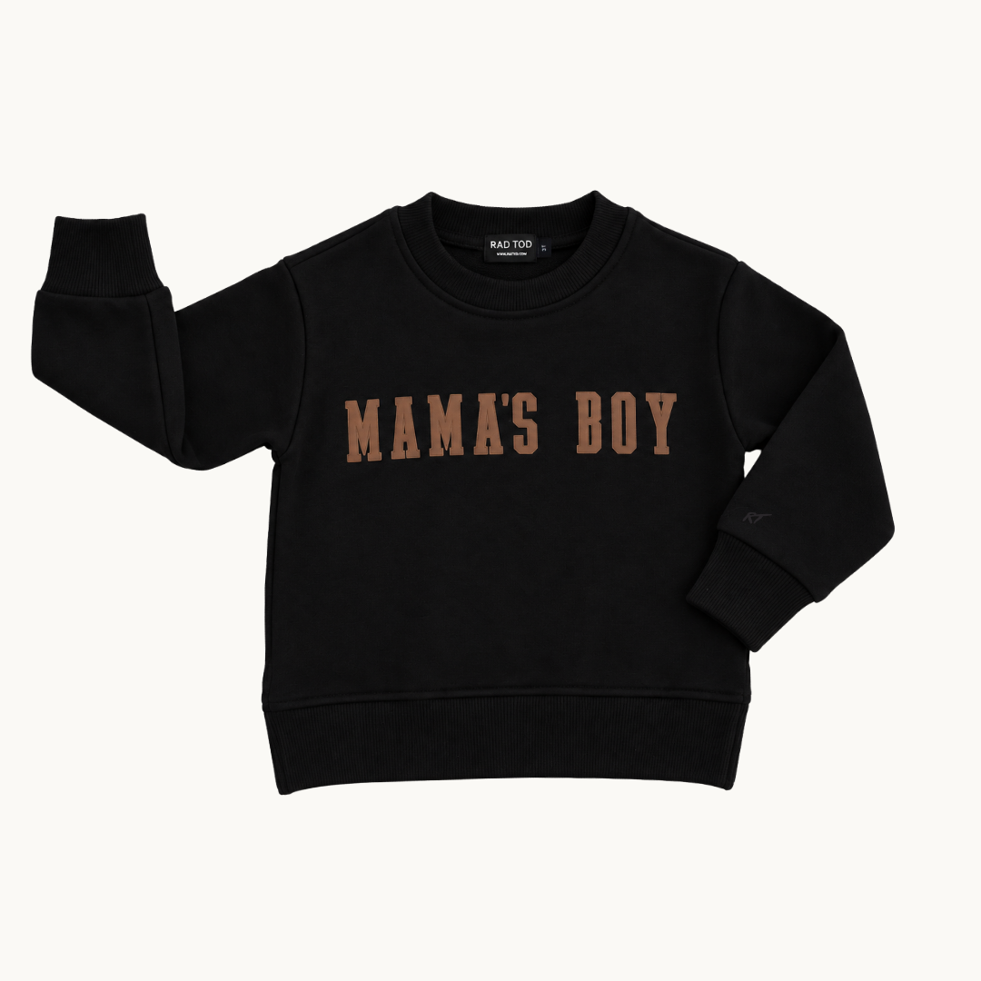 A black long-sleeve crewneck sweatshirt with 'MAMA'S BOY' printed across the chest in a distressed brown font, displayed flat against a light off-white background.