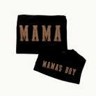 Two folded black crewnecks on a light cream background. The larger crewneck says 'MAMA' in tan varsity-style letters, and the smaller shirt says 'MAMA'S BOY' in the same tan lettering.