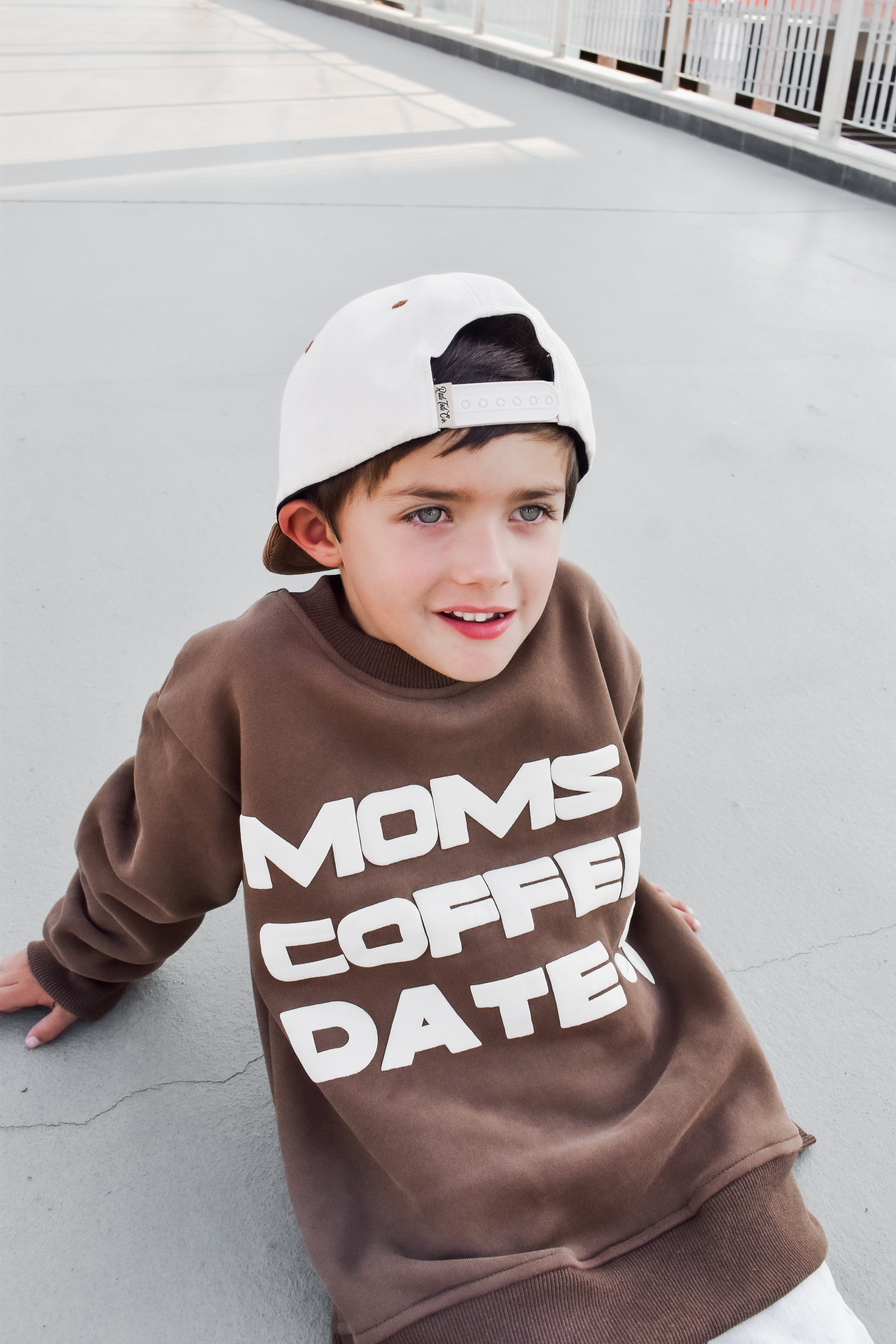 boy happily wearing coffee-brown “Mom’s Coffee Date” crewneck with bold off-white lettering, slightly oversized fit.