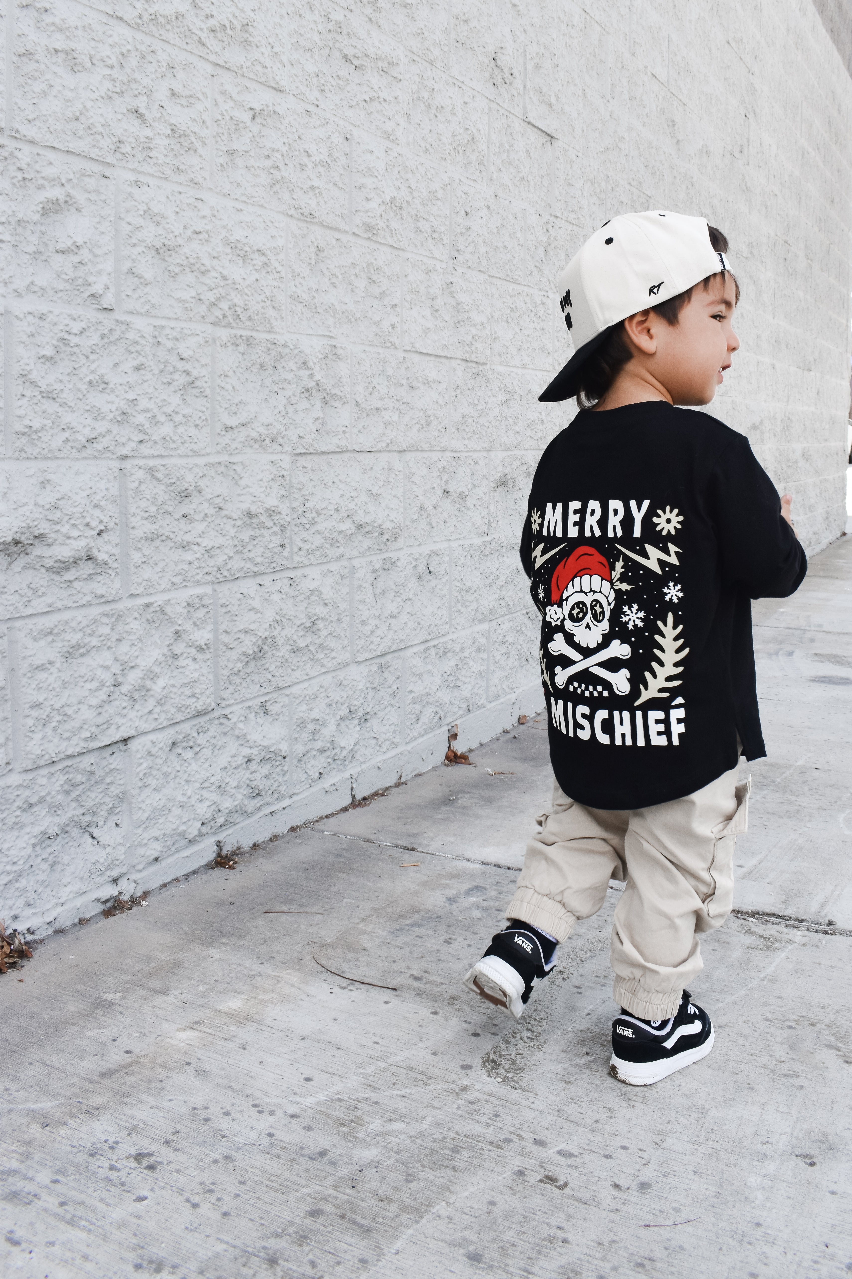 Child wearing a black t-shirt with a graphic design, walking on a sidewalk.