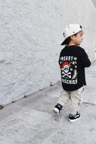 Child wearing a black t-shirt with a graphic design, walking on a sidewalk.