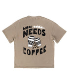 A beige short-sleeve t-shirt shown from the back, featuring a black graphic print that reads 'MOM NEEDS COFFEE' with two coffee cups and coffee beans.