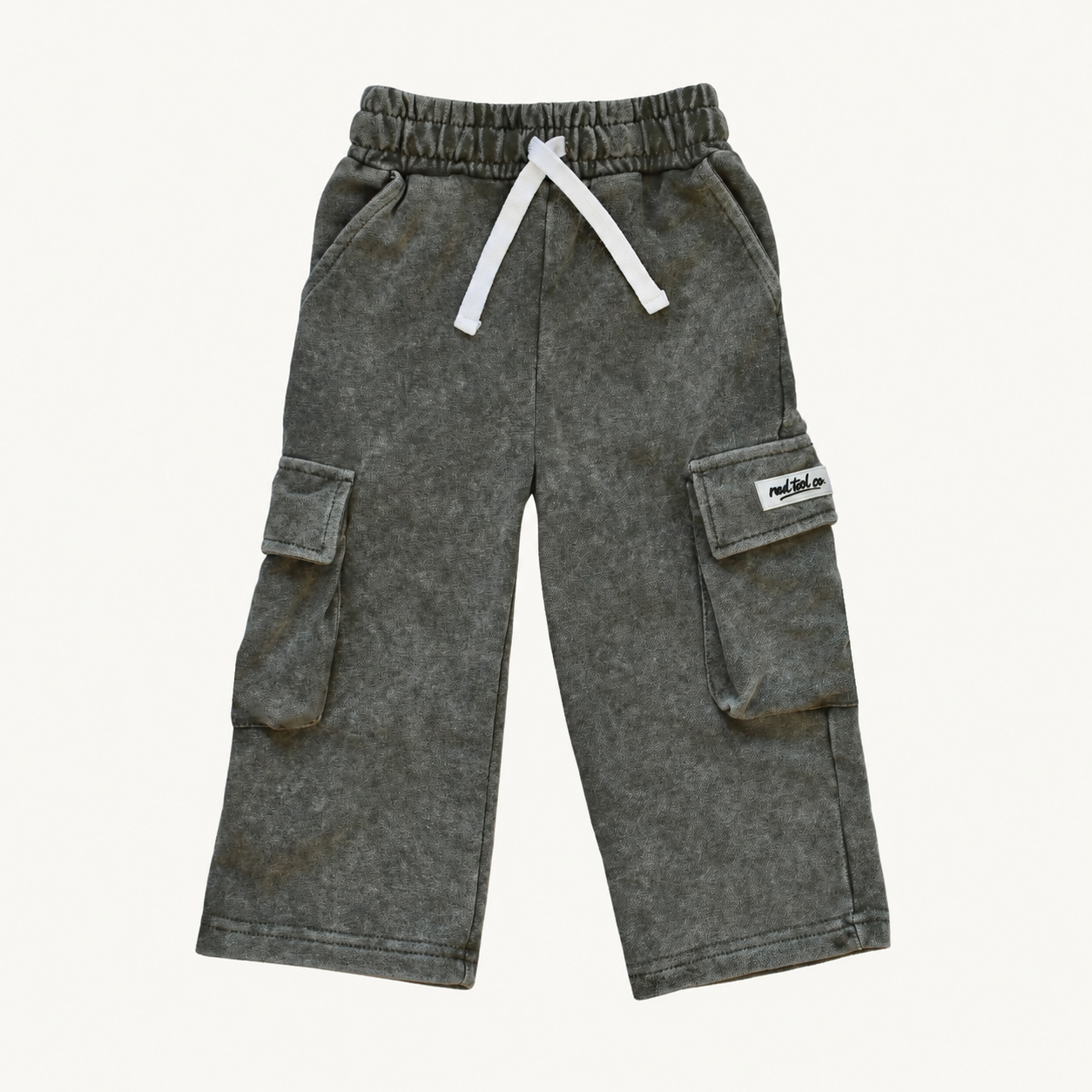 A pair of washed dark moss pants for kids, featuring an elastic waistband with a white drawstring and side cargo pockets, shown against a plain off-white background.