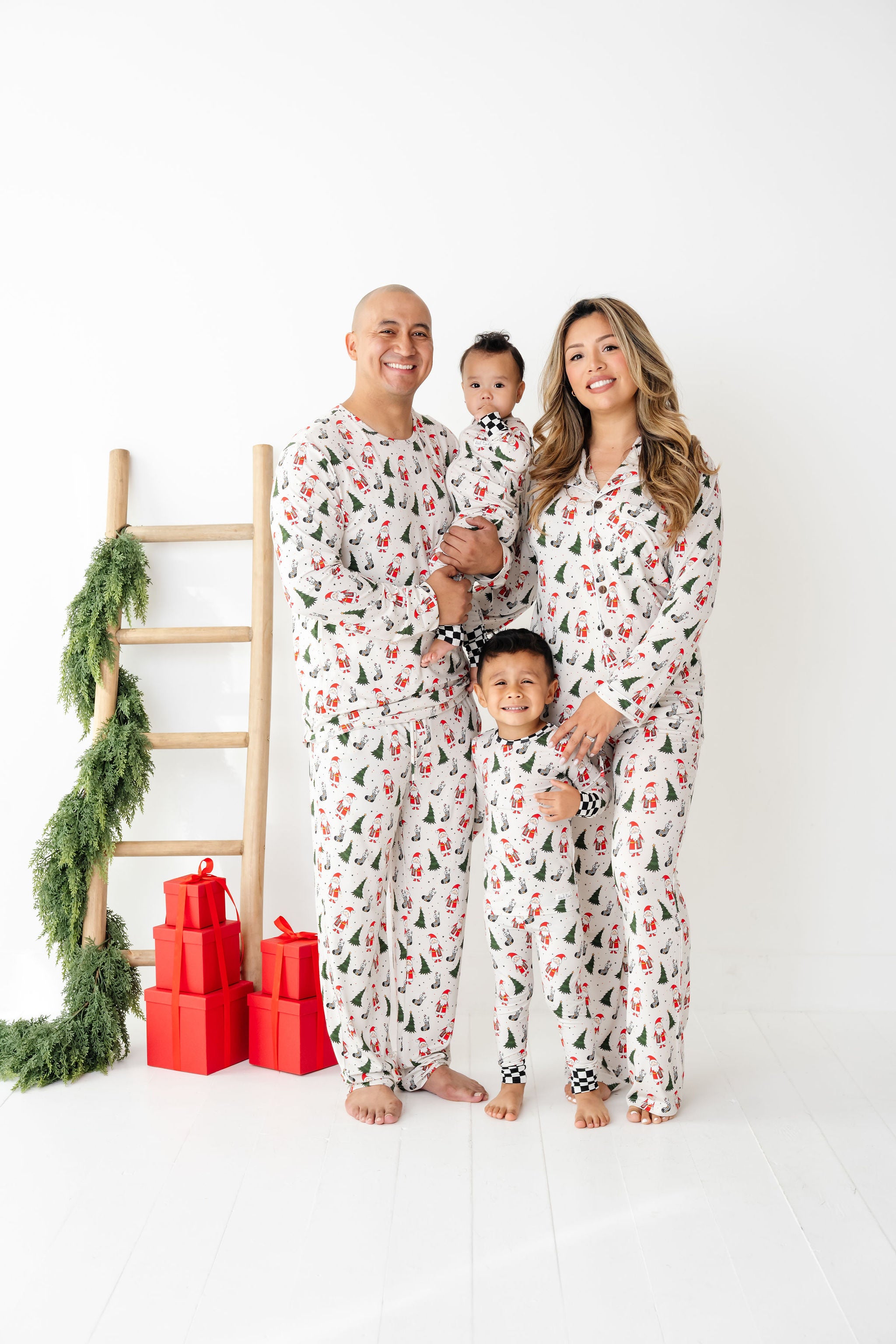 Family of four wearing matching pajamas with a Christmas tree and presents in the background while wearing Merry Everything Bamboo by RAD TODDLER
