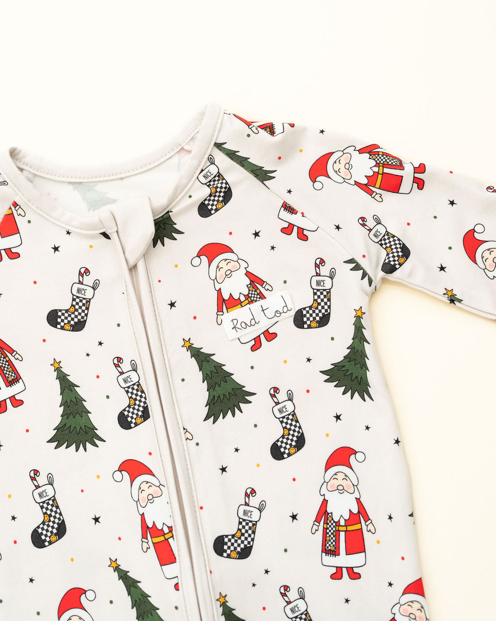 Baby onesie with Christmas-themed design featuring Santa Claus, trees, and stockings on a white background by RAD TODDLER