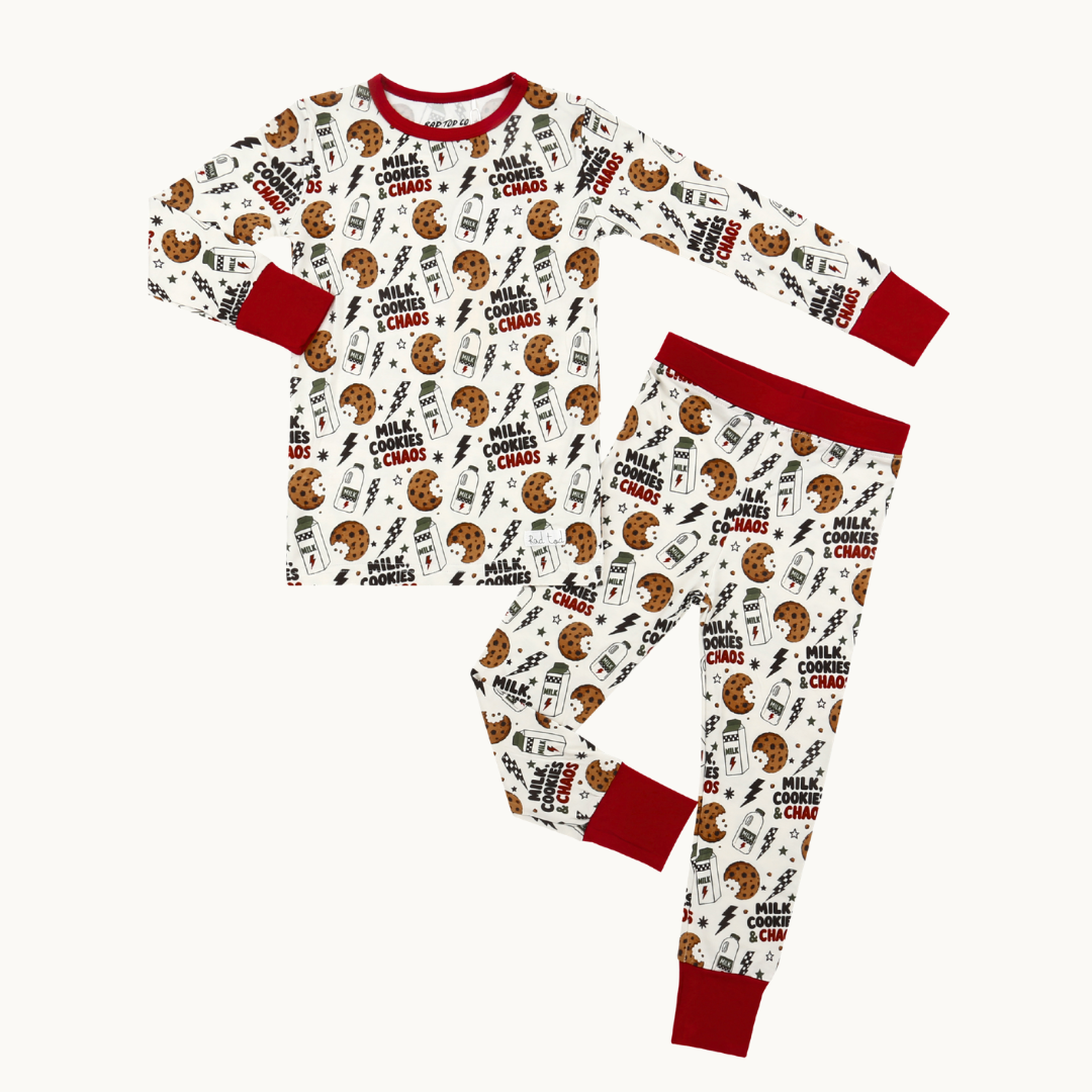 A two-piece pajama set featuring a long-sleeve top and matching pants with an all-over christmas and text print on an off-white background, finished with solid red cuffs, collar, and waistband.
