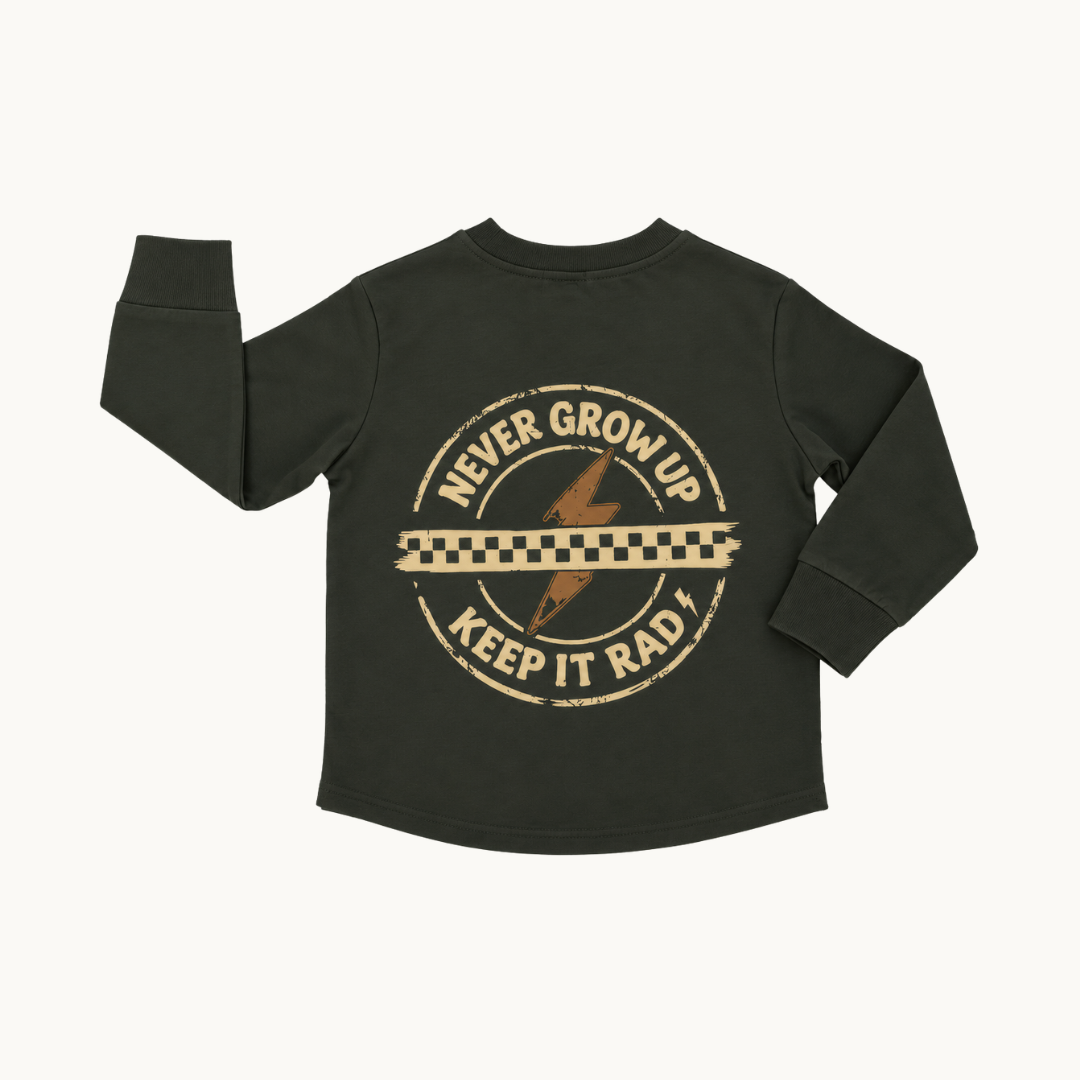 A dark green long-sleeve t-shirt with a distressed tan graphic on the back that reads 'NEVER GROW UP KEEP IT RAD!' with a lightning bolt and checkered stripe, shown on a light off-white background.