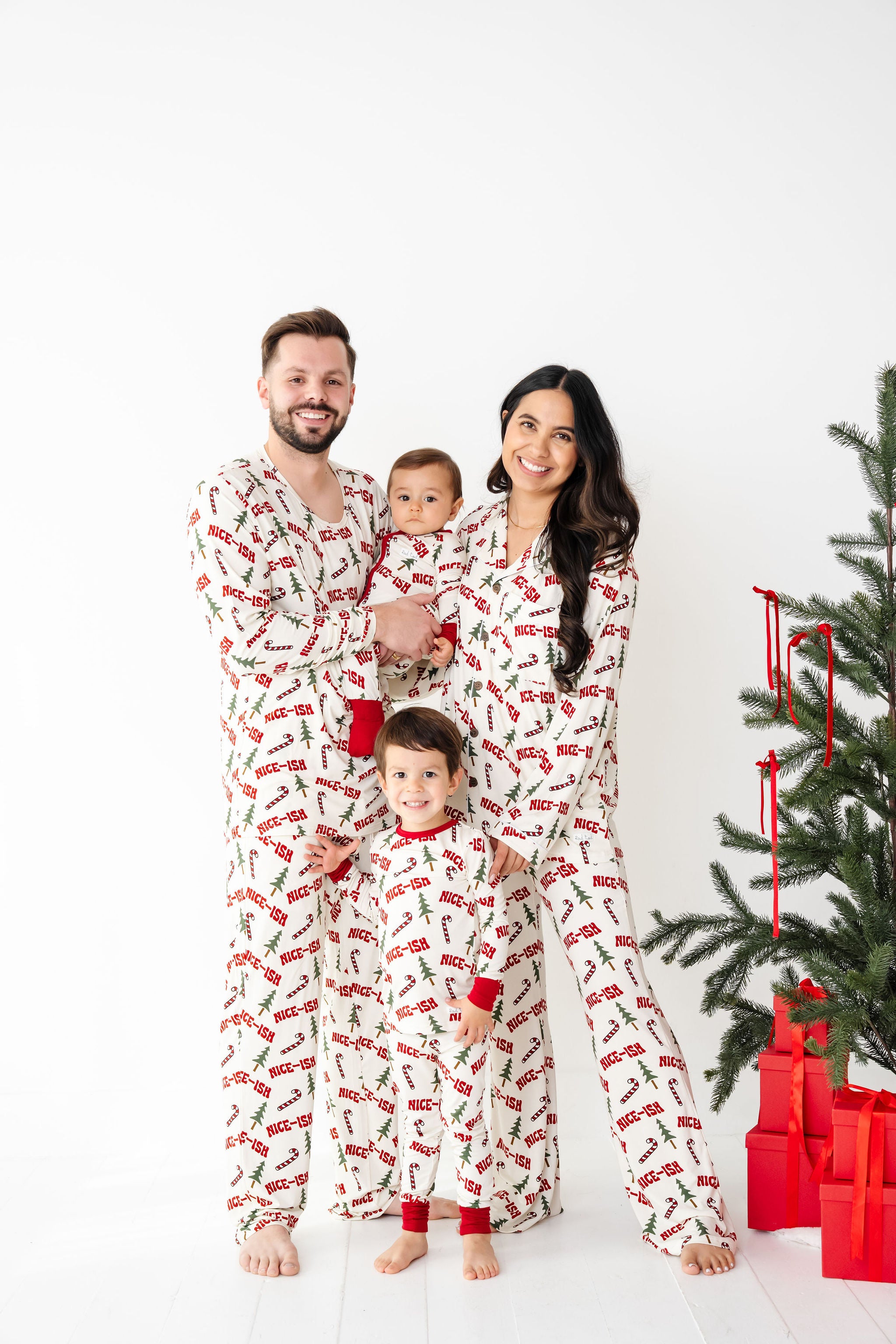 Family of four wearing matching pajamas in front of a Christmas tree with presents.