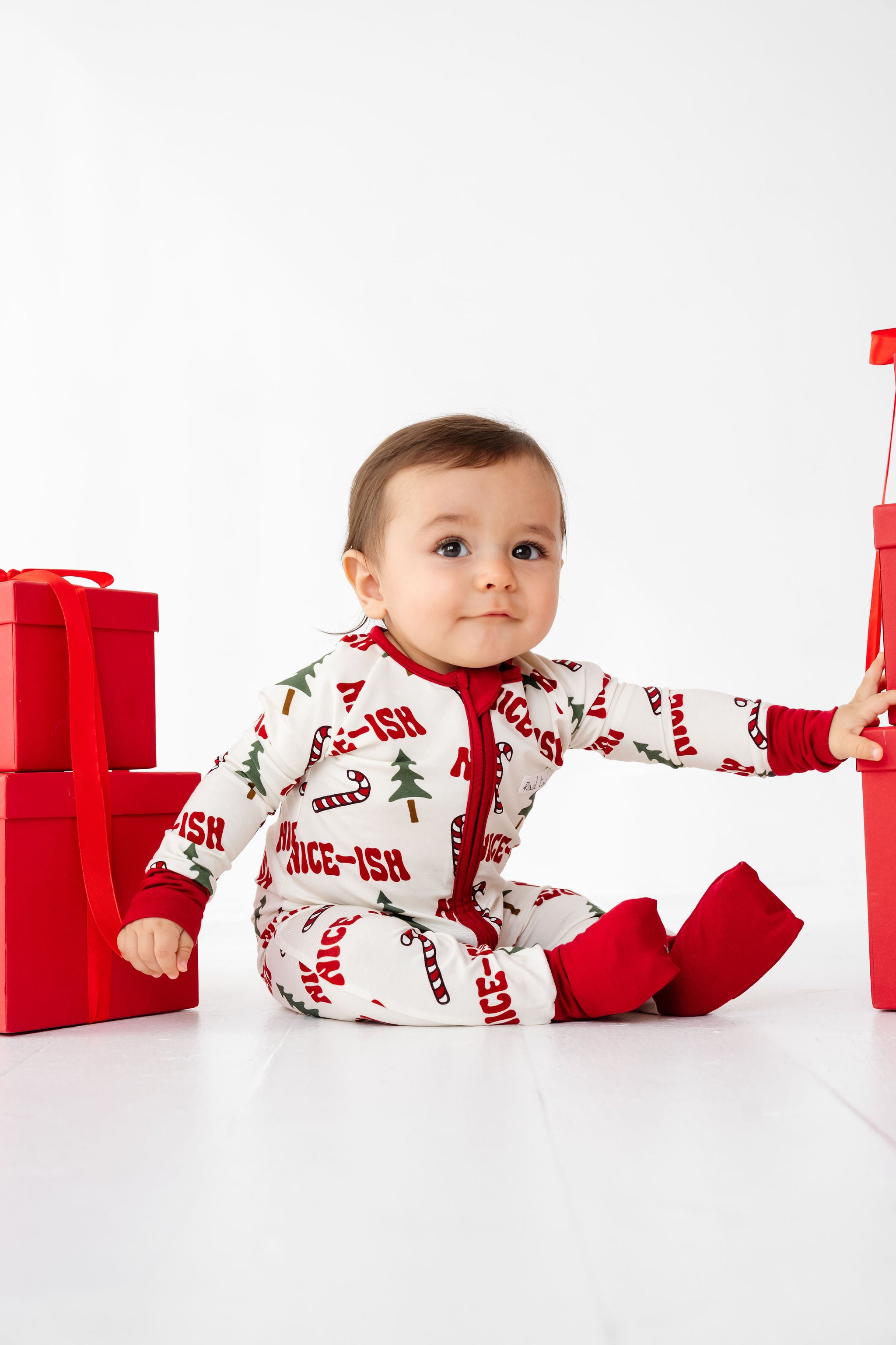 Baby in Christmas-themed outfit with presents on a white background