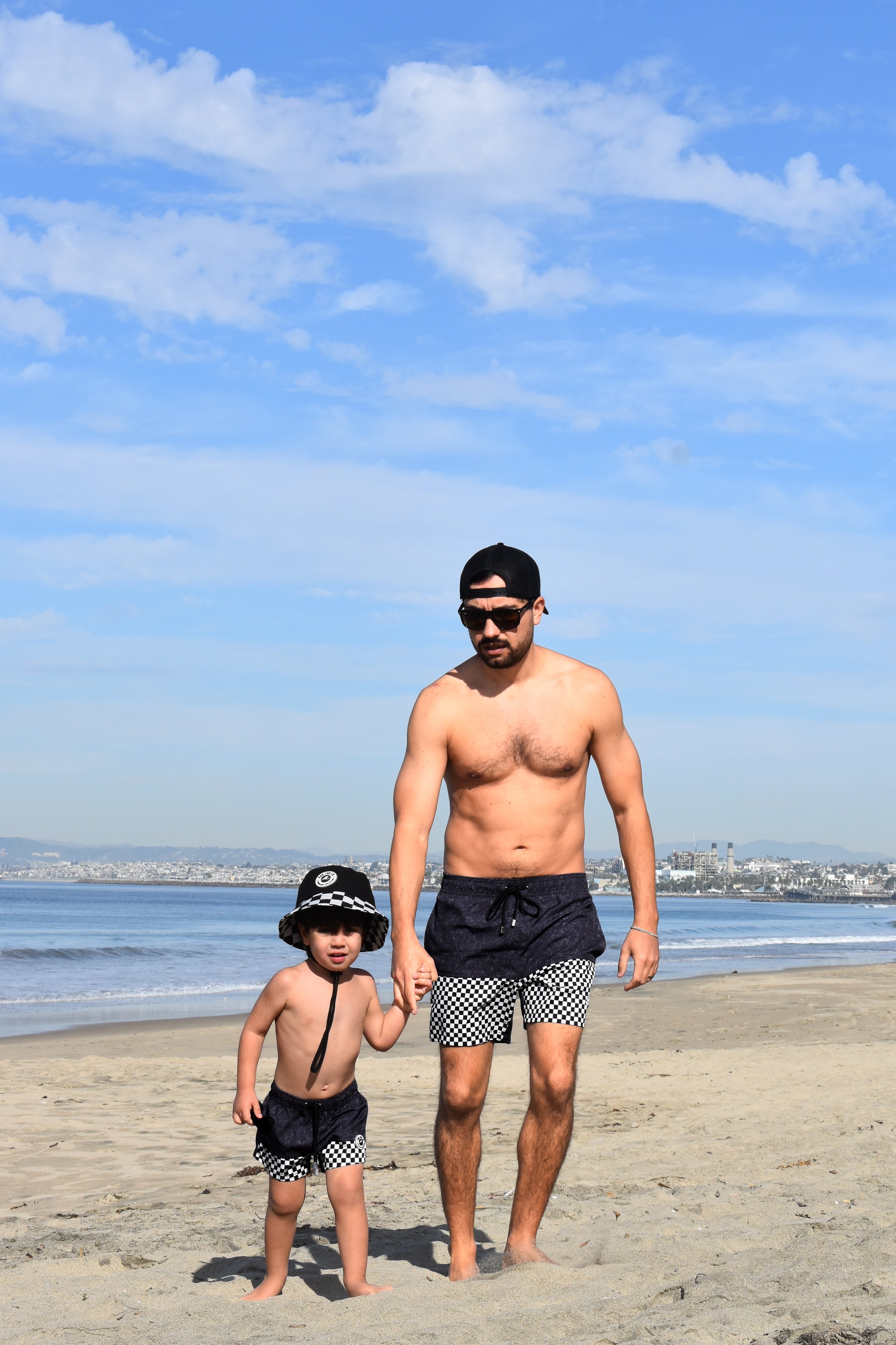 Man and child standing on a beach with ocean and sky in the background wearing matching Onyx Swimmie Shorts