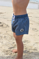 boy wearing rad toddler blue striped swim shorts on a sandy beach.
