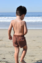 Child wearing brown striped swim shorts on a beach