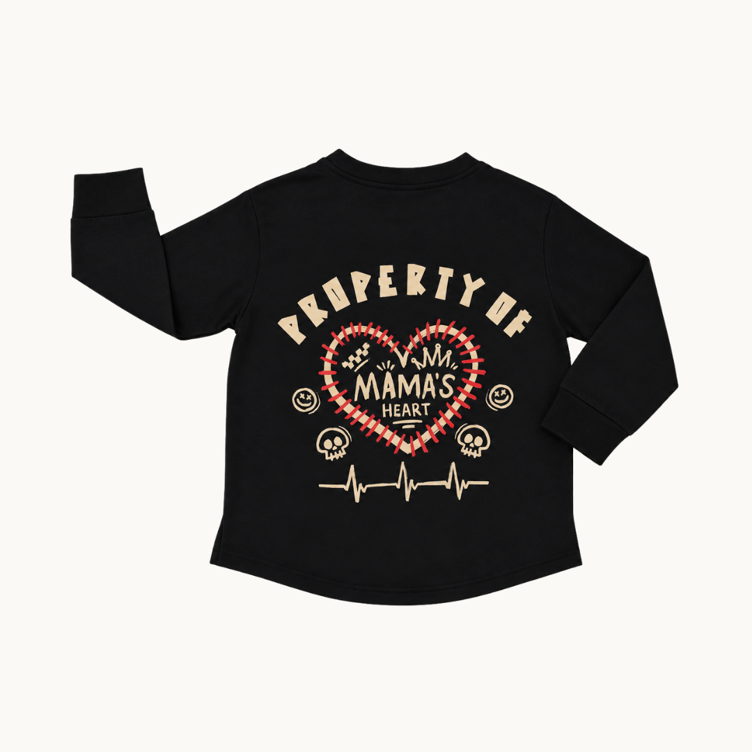 A black long-sleeve t-shirt with a graphic on the back featuring a red and white checkered heart, the words 'PROPERTY OF MAMA'S HEART' in beige, and small beige smiley faces and skull motifs, shown on a light off-white background.