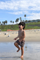 Child playing on a beach with seagulls and palm trees in the background while wearing Salty Bro Shorts by Rad Toddler