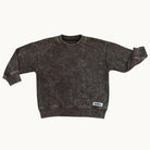 A dark brown acid-wash crewneck sweatshirt with rolled cuffs and a small white brand patch on the lower hem, displayed flat against a light cream background.