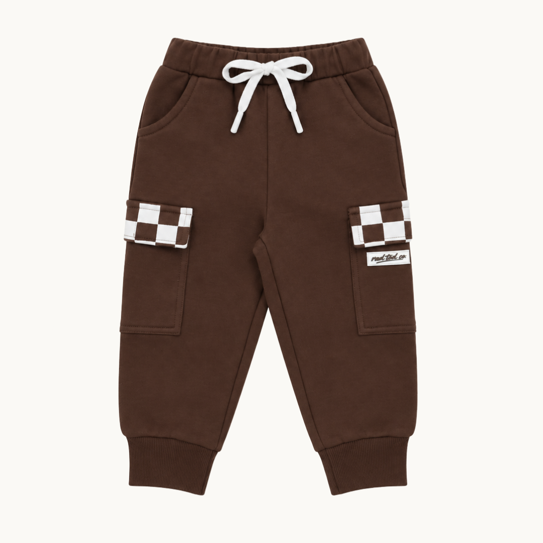 A pair of dark brown jogger pants for kids, featuring a white drawstring waist, side pockets, and cargo pockets with brown and white checkerboard patterns on the upper legs.