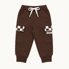 A pair of dark brown jogger pants for kids, featuring a white drawstring waist, side pockets, and cargo pockets with brown and white checkerboard patterns on the upper legs.