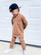 Young boy wearing almond Core Collection toddler crewneck with oversized fit, standing outdoors.