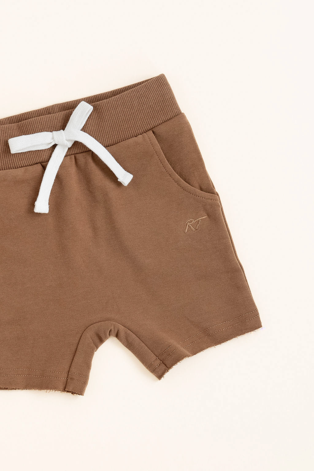 Flat lay of almond toddler shorts from the Core Collection with adjustable waistband and front pockets from the side.