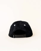 A black snapback cap shown from the back, featuring white embroidered eyelets and a black adjustable strap with a small white brand tag.