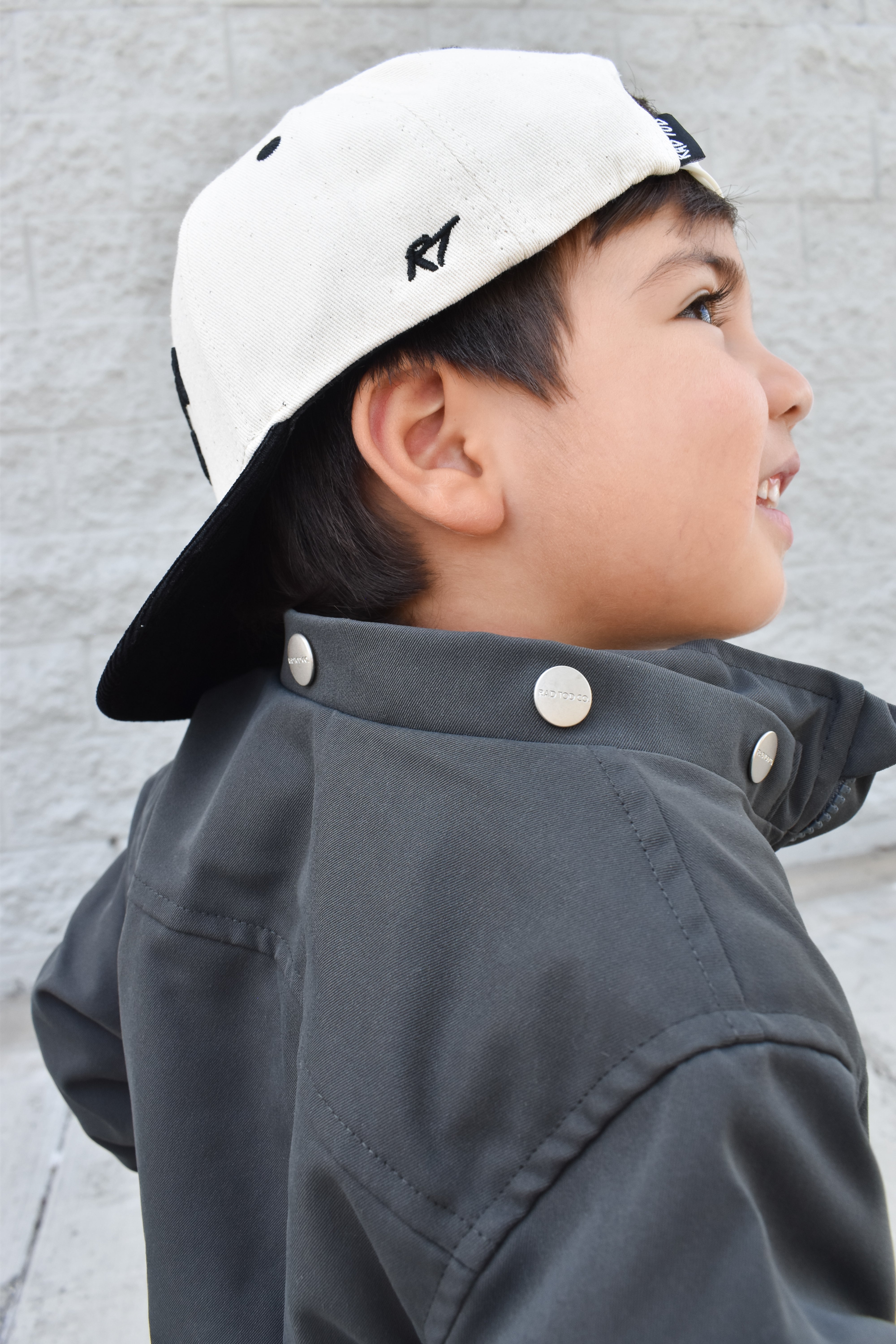 Child wearing a white cap and dark jacket against a light gray background