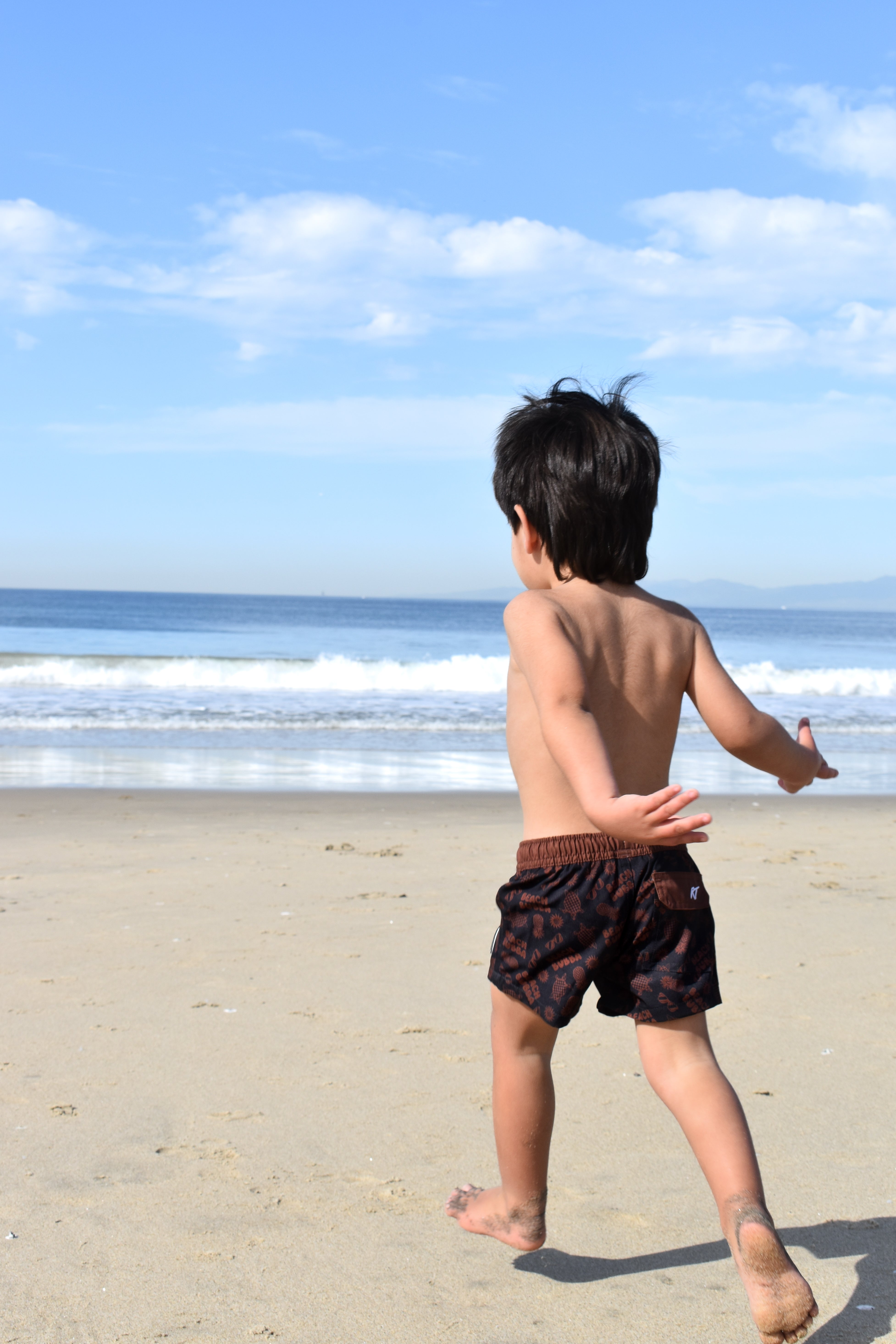 Child running on a sandy beach with ocean and blue sky in the background